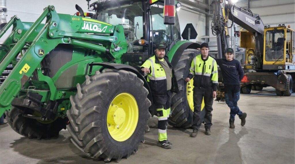 Kolme miestä seisoo vihreän traktorin vieressä.